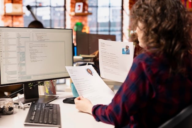 A close up of a person reviewing a resume. A computer monitor is visible in the background with a job site.